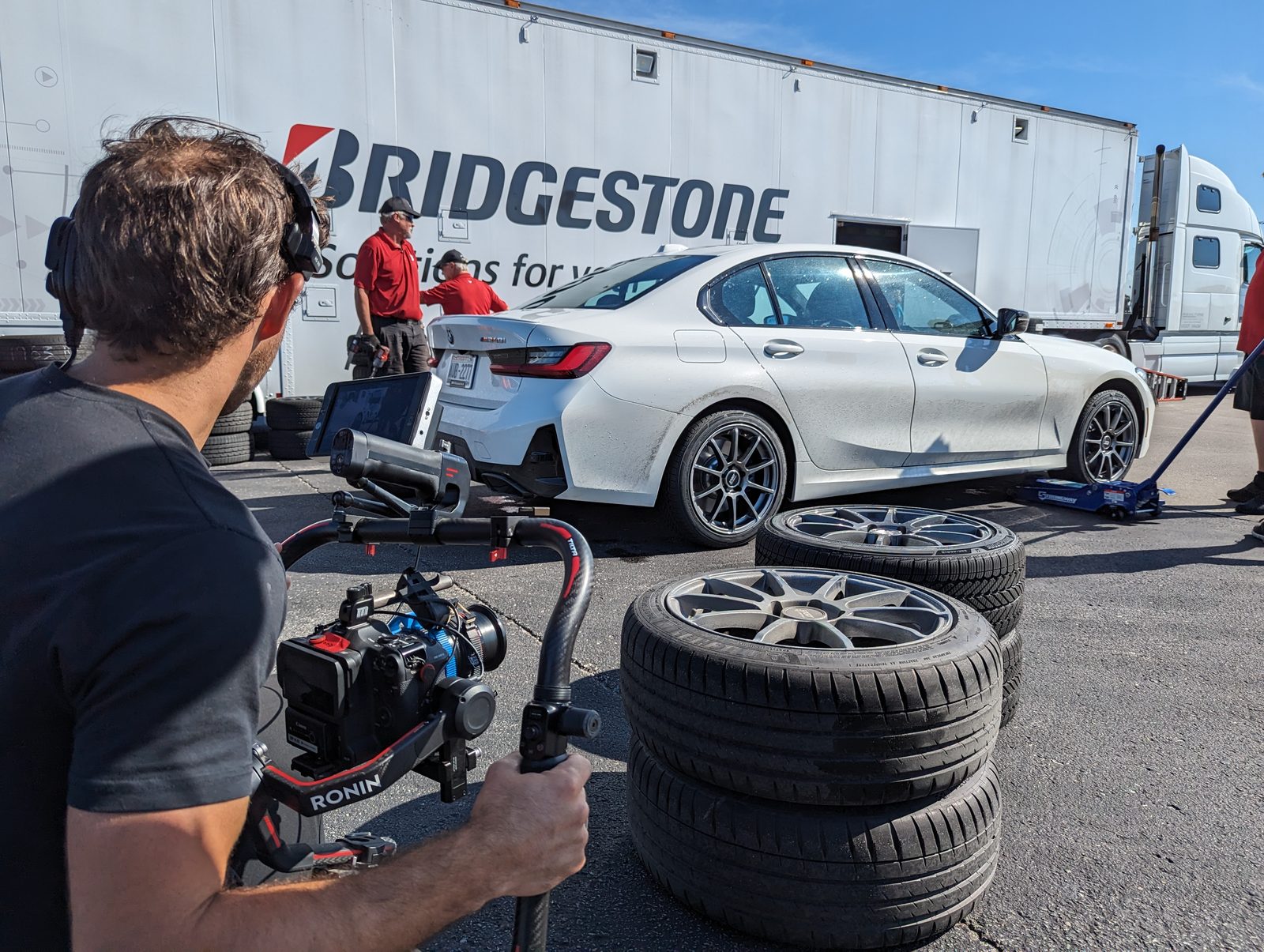 Tactiv operator running a gimbal rig on a Bridgestone tyre shoot, filming a white sedan on jacks beside the branded team transporter