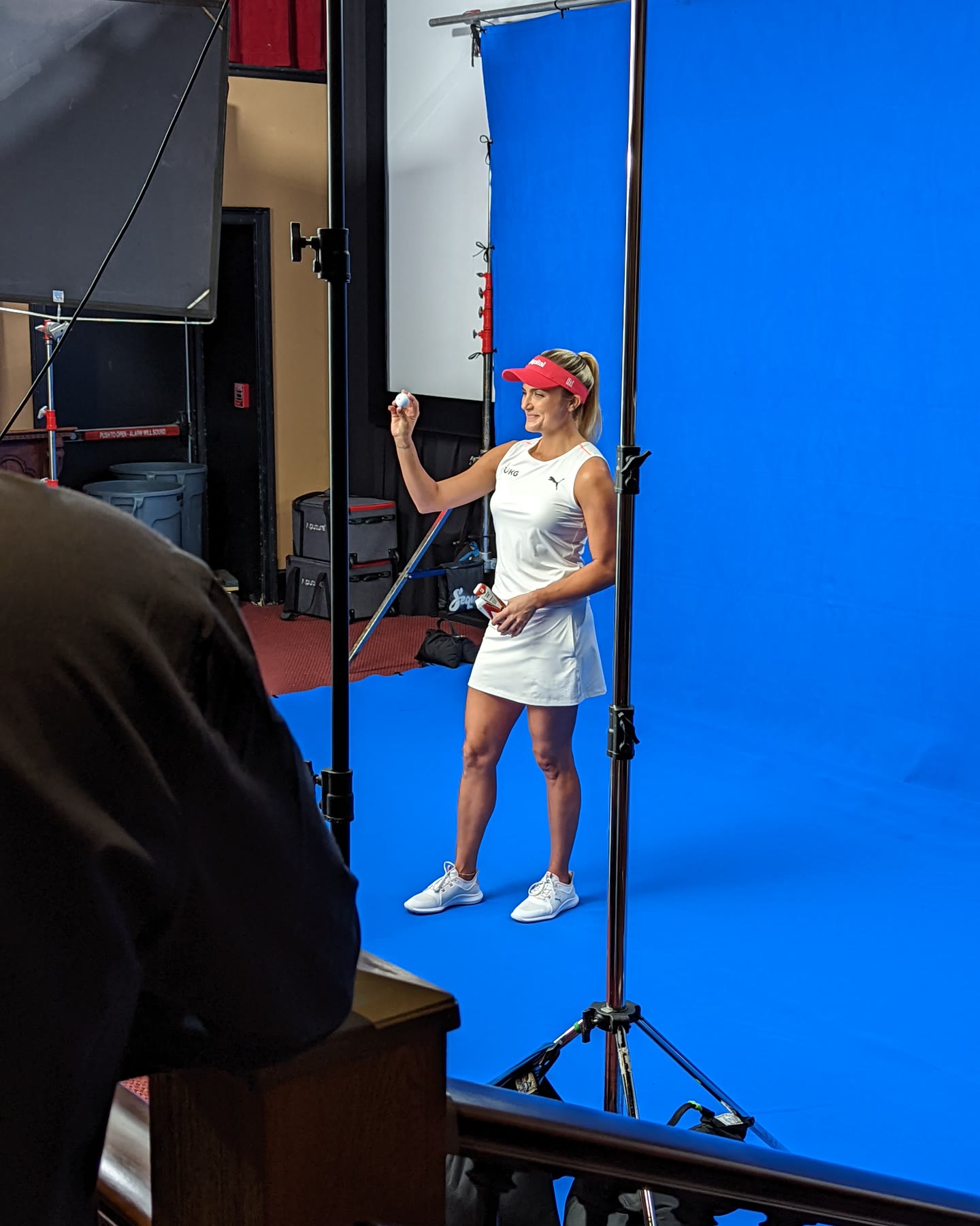 A golf professional holds a ball up to camera on the blue-screen set built inside a theater for a Bridgestone Golf shoot, a large softbox at camera left and C-stands marking her position