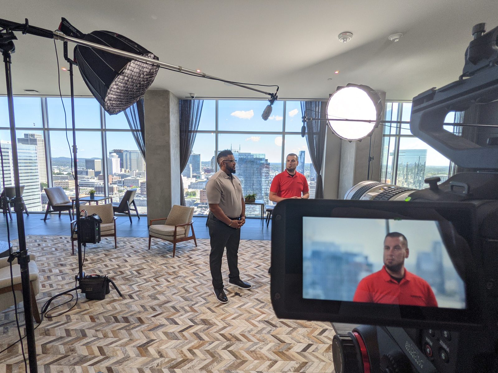 Two spokespeople on camera in a high-rise lounge overlooking the Nashville skyline, framed by a softbox, boom microphone and the operator's monitor