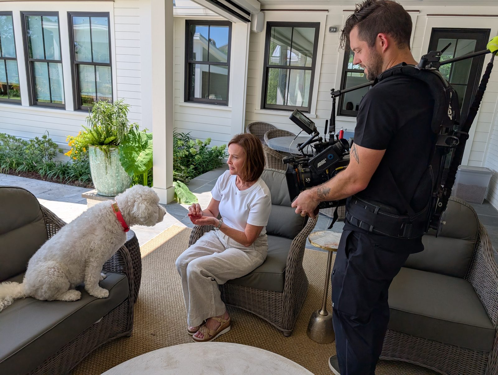 Camera operator in a stabilising vest filming a woman and her dog on a covered porch during a lifestyle shoot