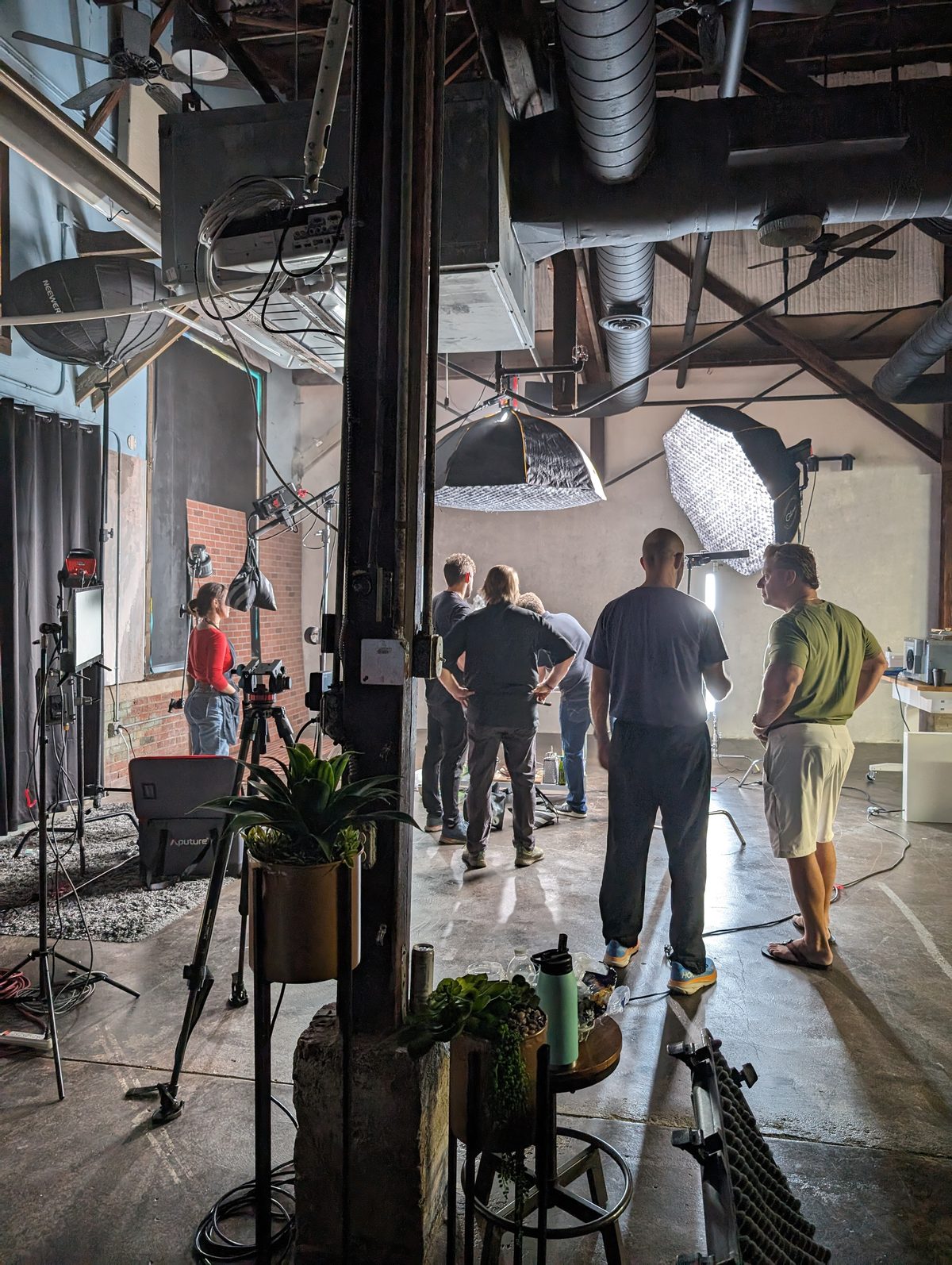 Wide view of a Tactiv studio build in a brick warehouse: crew of five around a large octabox and grid softbox rigged over the set