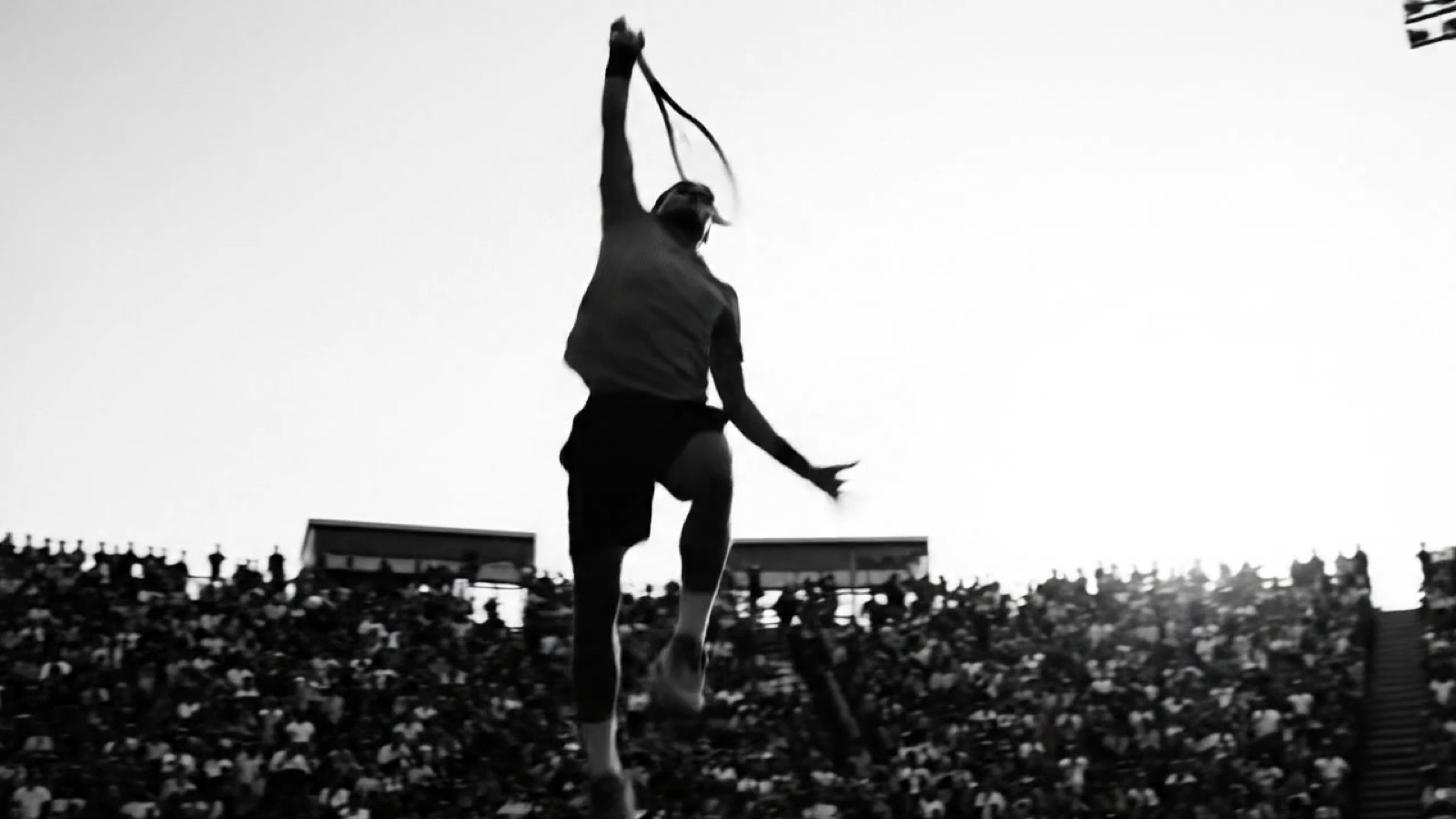 Black-and-white frame from a Tactiv stadium commercial: tennis player mid-serve before a packed crowd