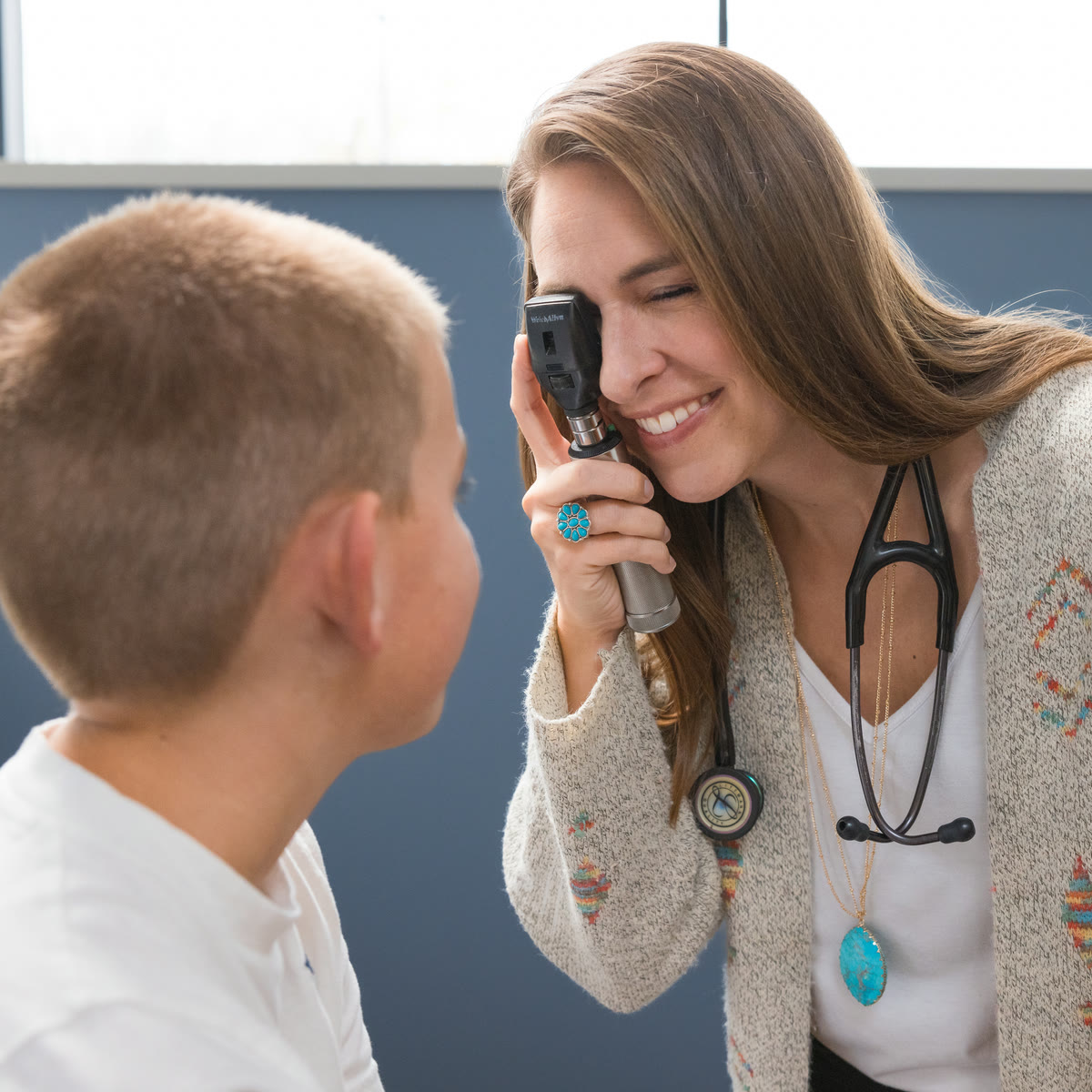 ADENA Health campaign still: a smiling paediatric clinician checks a young boy's ear with an otoscope in a bright exam room