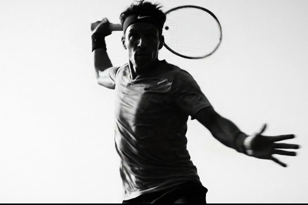 Black-and-white commercial frame: a tennis player follows through on a forehand against a blown-out white studio background